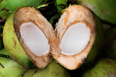 Fresh young coconut split in half showing white flesh with pile of coconutsの写真素材