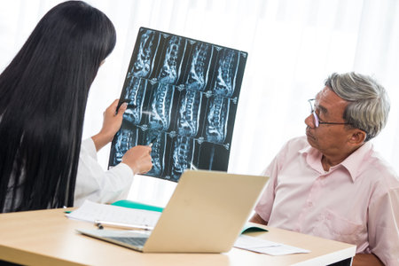 Expert doctor examining and explaining x-ray film to elderly patient in medical office