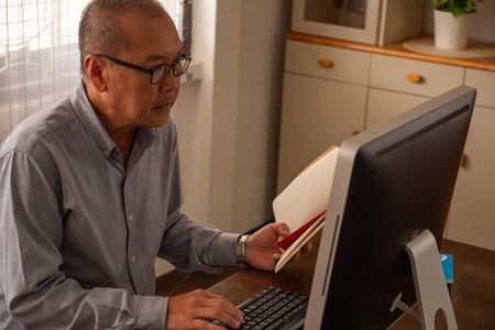 Asian businessman typing on a computer keyboard and holding a book in the office room.の写真素材
