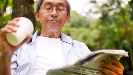 Asian man drinking coffee and reading newspaper at the park.の写真素材