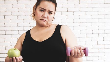 Asian chubby woman standing and holding apple and dumbbell.の写真素材