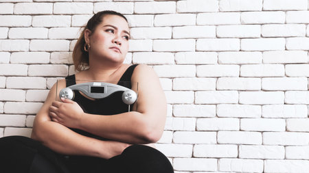 Beautiful chubby woman holding a weighing apparatus and sitting in a room.