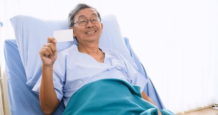 Male patient smiling and holding card on sickbed in hospital room.の写真素材