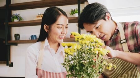 Happy gardener couple taking care of yellow flowers together in the room.の写真素材