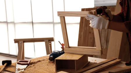 Carpenter using drill to screwing pieces of board at site.