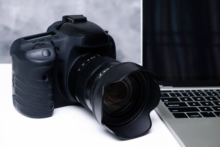 A black digital camera and a computer laptop on a tableの写真素材