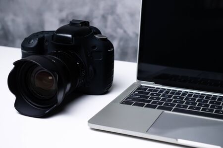 A black digital camera and a computer laptop on a table.の写真素材