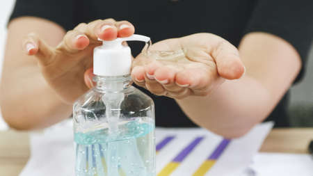 Business woman cleaning hands with sanitizer alcohol gel while working on her desk.の写真素材