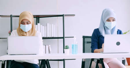 Muslim businesswomen wear protective masks and clean hands with sanitizer alcohol gel during work in office.の写真素材