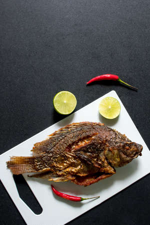 Fried fish on white chopping block with black backgroundの写真素材