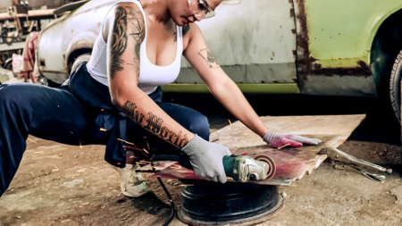 Attractive young woman mechanical worker repairing a vintage car in old garage.の写真素材