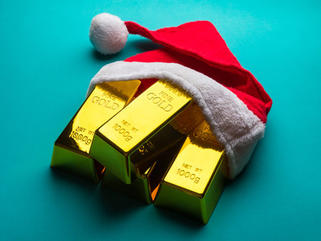 Gold bars as christmas present with Santa hat on green background.の写真素材