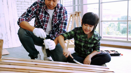 Young male carpenter teaching his son how to work with wood in workshop.の写真素材