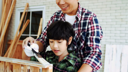 Young male carpenter teaching his son how to work with wood in workshop.の写真素材