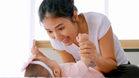 Young mother with her little baby playing on bed at home.の写真素材