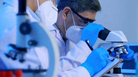 Two Asian scientists doing some research and looking through a microscope in laboratory.