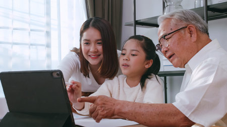 Grandfather and mother are teaching daughter homework while studying online at home.
