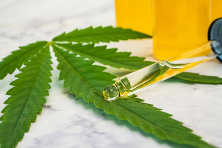 Cannabis oil in the vials with dropper tube and green leaf on marble table. Alternative medicine...