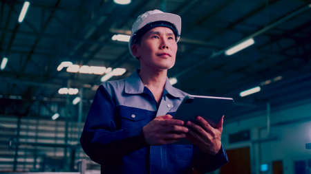 Engineer is using a tablet to check the machine's control system in a factory.の写真素材