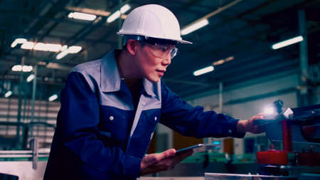 Engineer is using a tablet to check the machine's control system in a factory.の写真素材