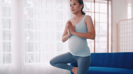 Asian pregnant woman doing yoga exercises at home.の写真素材