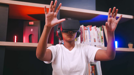A schoolgirl sitting in front of library's bookshelf and using virtual reality glasses.