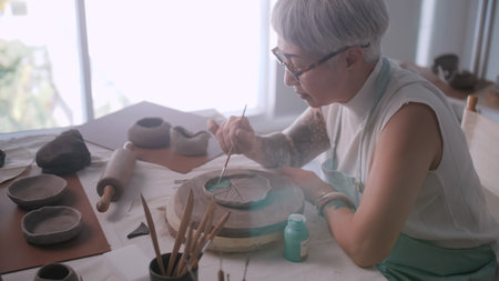 Asian elderly woman enjoying pottery work at home. A female ceramicist is making new pottery in a...