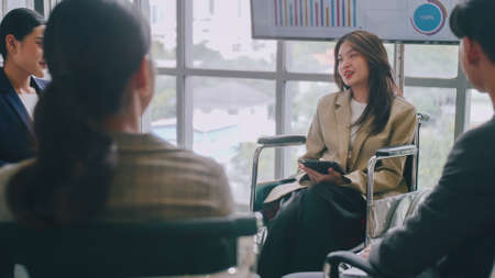 Confident business woman in wheelchair presenting during business meeting with colleagues.の写真素材