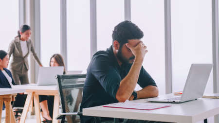 A young company employee is feeling tired while sitting at work for a long time.の写真素材