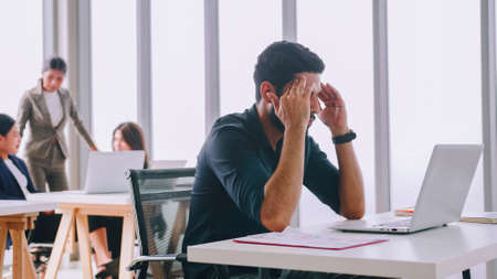 A young company employee is feeling tired while sitting at work for a long time.の写真素材