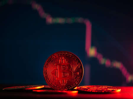 Coins with bitcoin symbol on red light and crypto stocks chart background. Concept of a cryptocurrency market crisis.の写真素材