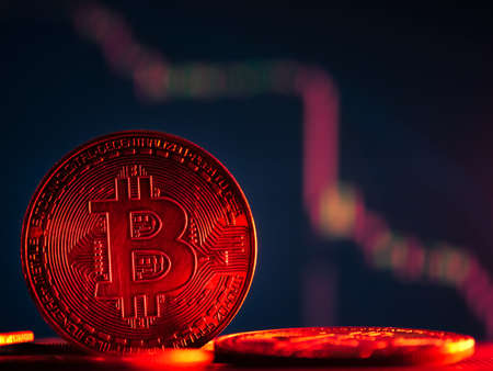 Coins with bitcoin symbol on red light and crypto stocks chart background. Concept of a cryptocurrency market crisis.の写真素材