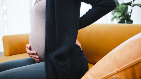 Asian pregnant woman has back pain while lying on sofa.