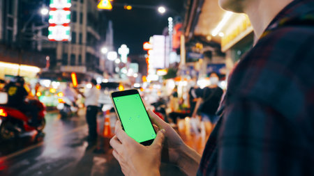 Female tourist holding smart phone with green screen display while standing on the street at night.の写真素材