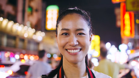 Portrait of a beautiful woman standing and smiling on the street of city at night.の写真素材