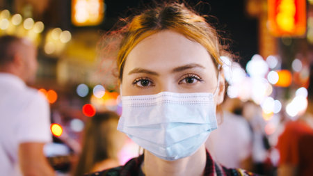 Portrait of a tourist woman wearing medical mask while standing on the street of city at night.の写真素材