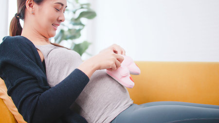 Beautiful Asian pregnant woman is preparing clothes for her newborn baby.
