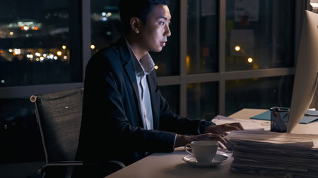 A young businessman concentrating on an analysis of work projects in his office until late at night.の写真素材