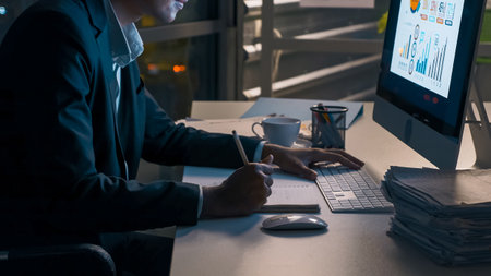 A young businessman concentrating on an analysis of work projects in his office until late at night.の写真素材