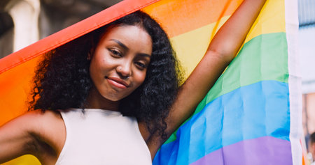 A young black woman waves a rainbow flag, a symbol of homosexuality, during a pride parade.の写真素材