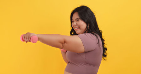A chubby Asian woman wearing exercise clothes is showing off her physical strength on a yellow...