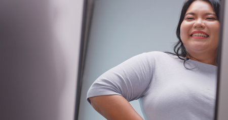A chubby Asian woman feels confident and proud of her body while standing in front of the mirror.の写真素材