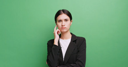 A young business woman is standing and thinking about something. Isolated on green background in...