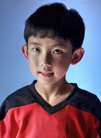 Asian boy wearing a sports jersey posing in studio, with special lighting to one side  Isolated on...