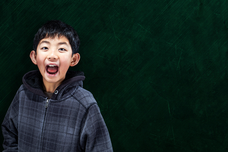 Smart Asian boy with in classroom setting with chalkboard background and copy spaceの写真素材