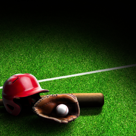 Baseball helmet, bat, glove and ball on grass field with marking. Dramatic spot lighting effect and copy space.の写真素材