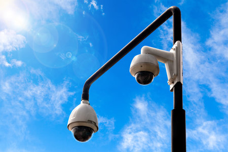 Outdoor street security cameras with blue sky background and lens flare from the sun. Copy space.