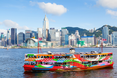 HONG KONG - JULY 10, 2017: A colorful Star Ferry approaches a ferry terminal at Tsim Sha Tsui in Hong Kong. The city's iconic Star Ferry carries passengers across Victoria Harbour between Hong Kong Island and Kowloon since 1888. The modern skyscrapers of のeditorial素材