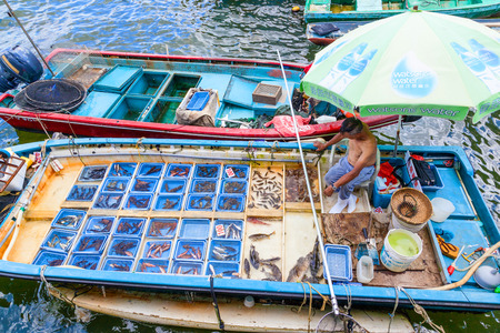 HONG KONG - JULY 13, 2017: A fisherman separates his live seafood catch into plastic containers on a boat at Sai Kung's floating seafood market. Every day, fishermen in boats alongside the Sai Kung harbor sell their fresh seafood to the public on the pierのeditorial素材