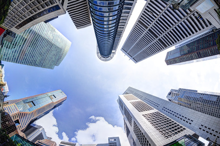 Bottoms-up view of business office skyscrapers and highrise buildings in Singapore's business and financial district at Raffles Place. Fisheye shot of rising architecture into blue and cloudy skies.の写真素材